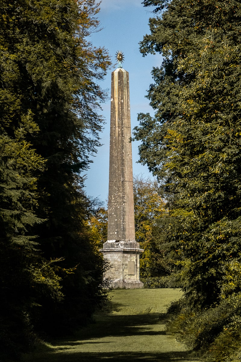 A large stone obelisk between two rows of trees