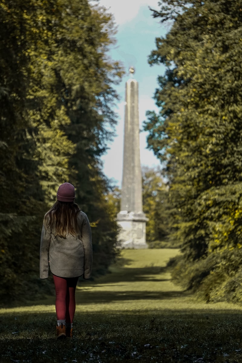 A woman admiring an obelisk structure between two rows of trees