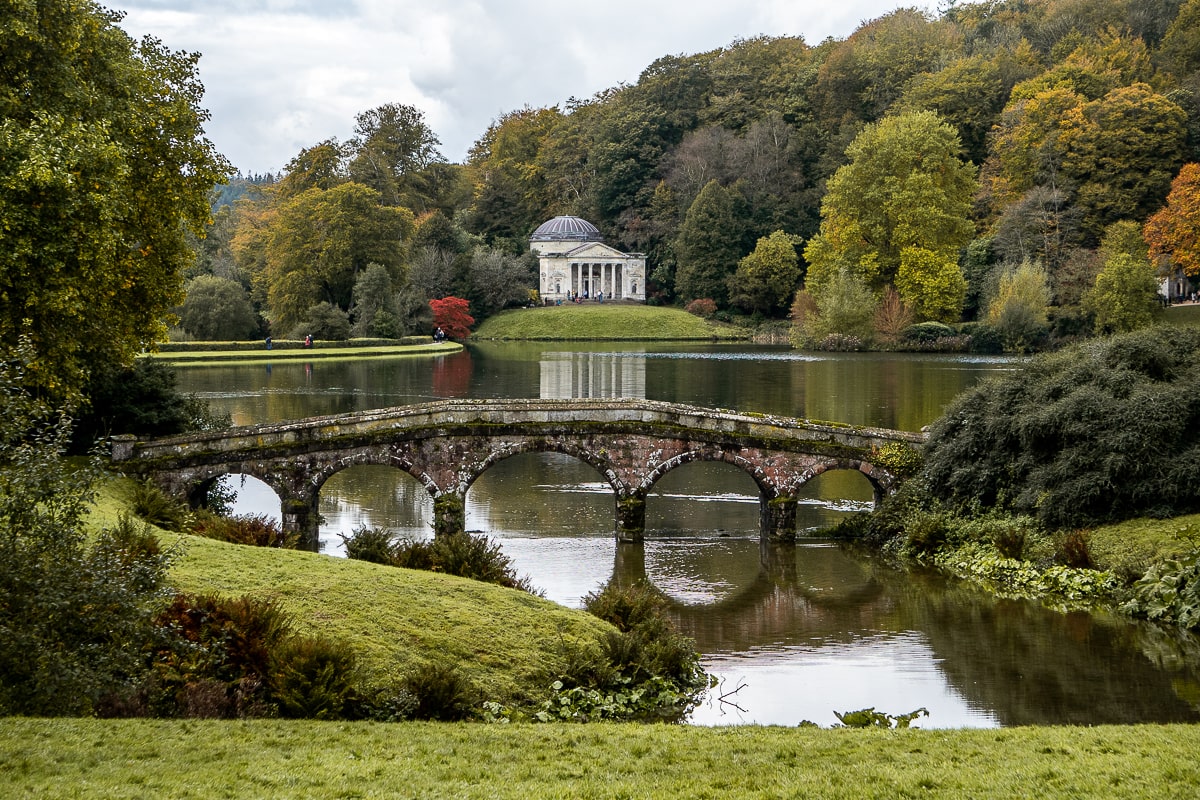 A Palladian bridge over a lake with a pantheon in the background