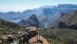 A panoramic view of Blyde canyon and the three rondavels - a group of distinct hills - and a couple stood on a rocky outcrop