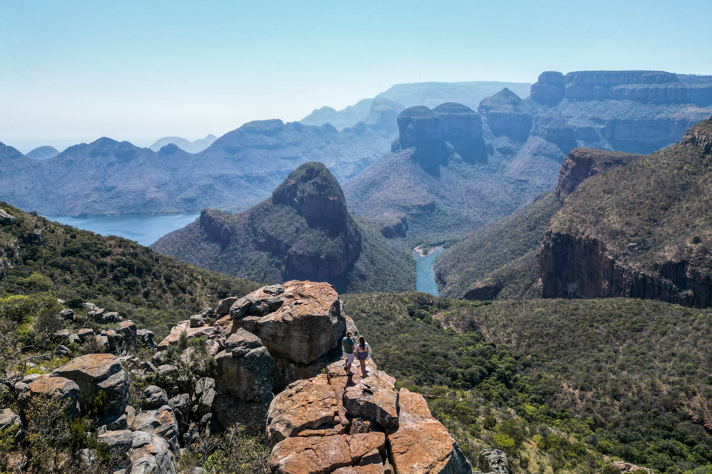 A panoramic view of Blyde canyon and the three rondavels - a group of distinct hills - and a couple stood on a rocky outcrop