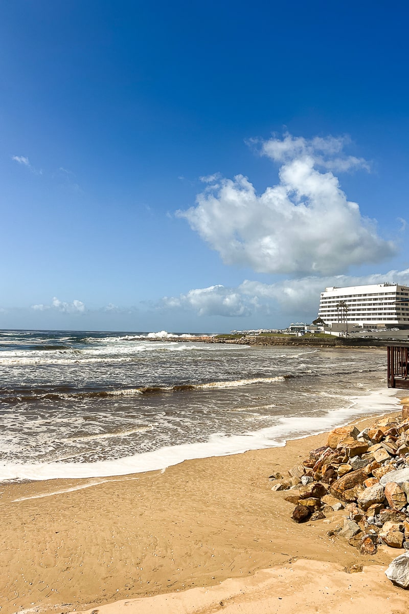 A sandy shore and sea with a white hotel