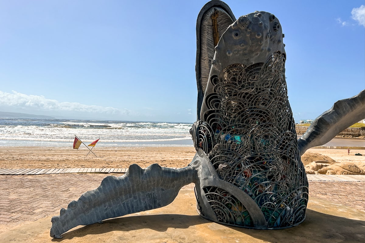 A large humpback whale statue made from metal items on the beach