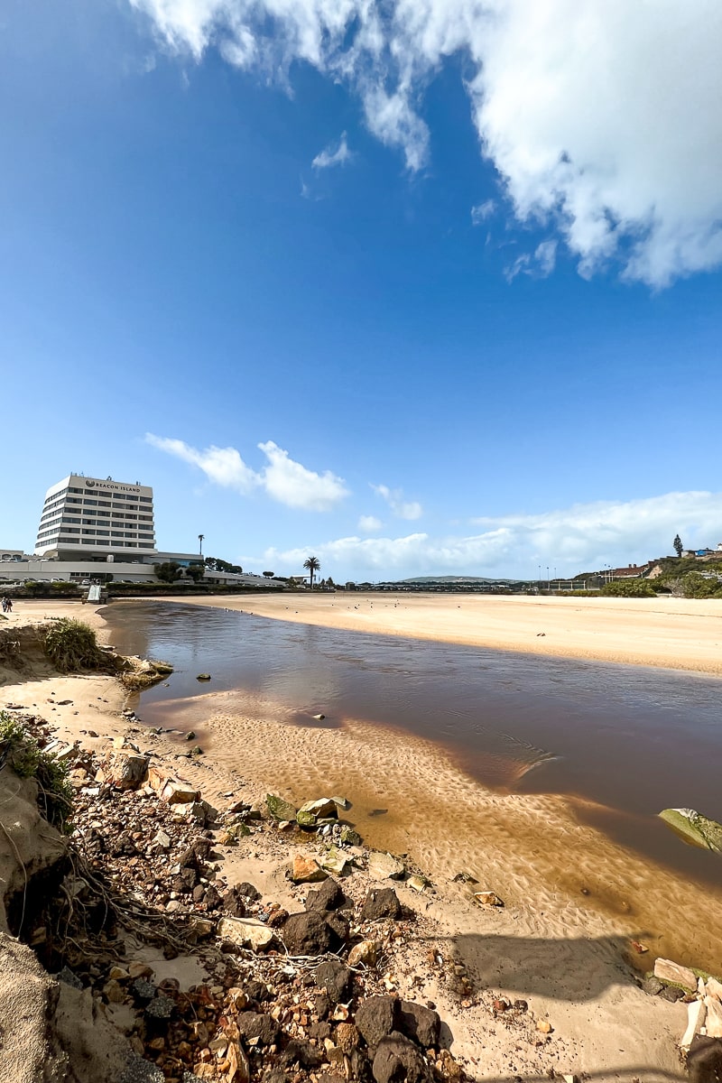 A river of water running through the beach and a white hotel in the background