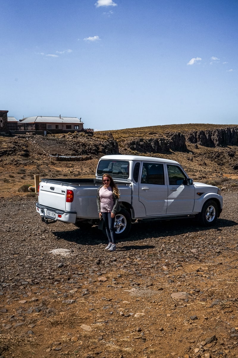 A woman standing next to a 4x4 pickup truck on a gravel road