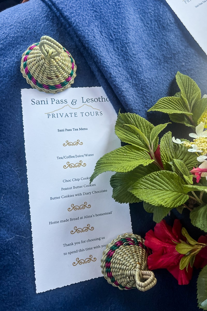 A tea menu for Sani Pass Private Tours with souvenir miniature Lesotho hats and a bouquet of flowers