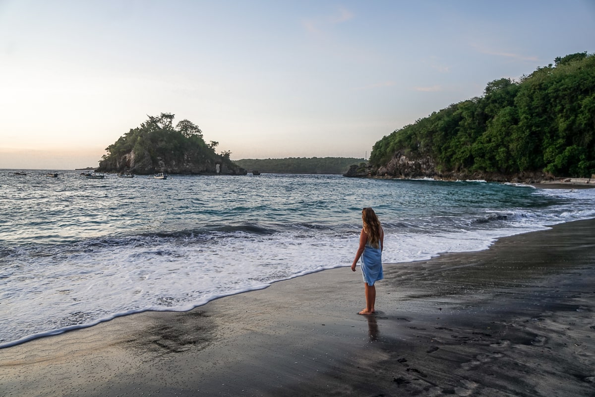 A woman looking out over the ocean at sunset on a sandy beach, surrounded by cliffs