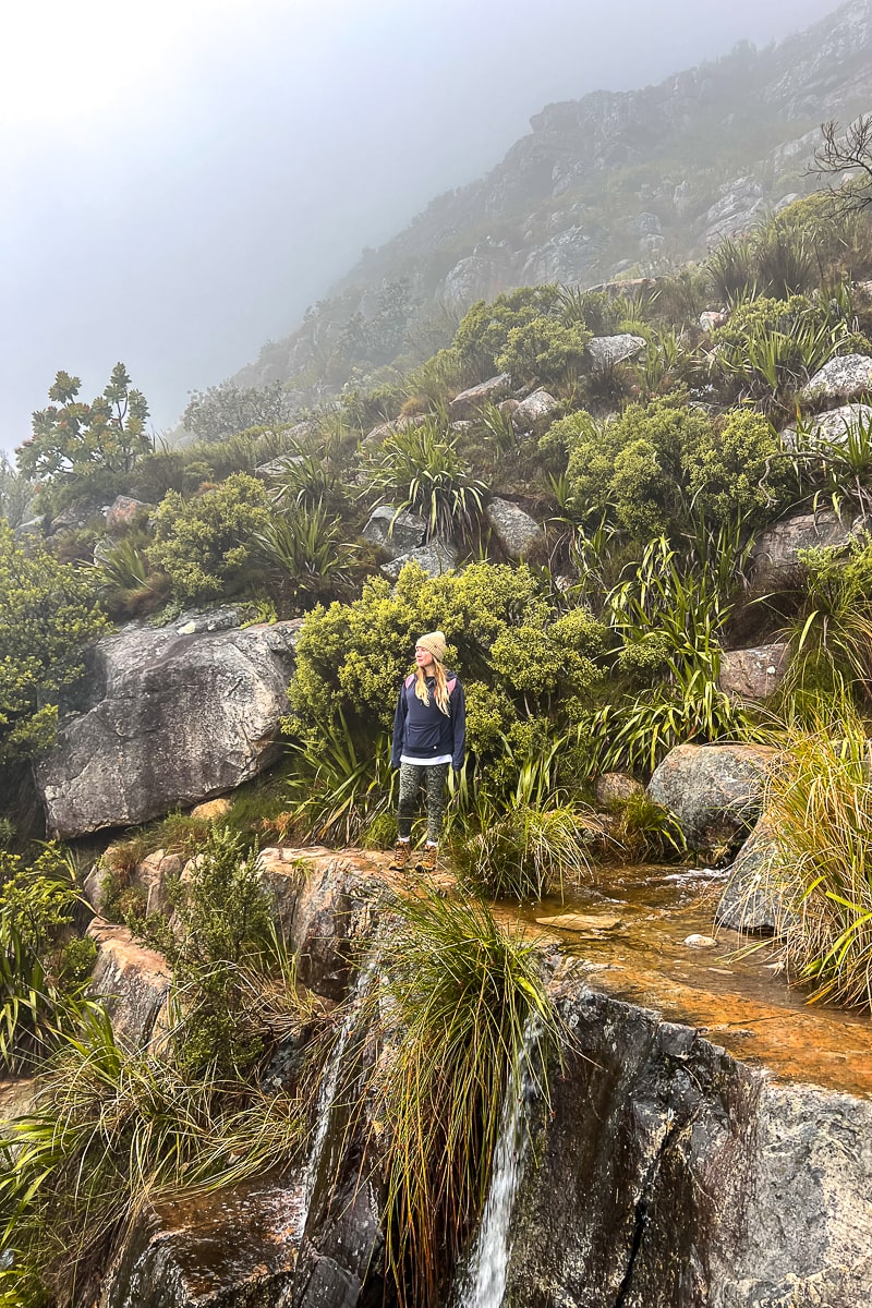 A woman on a rocky waterfall with green vegetation around