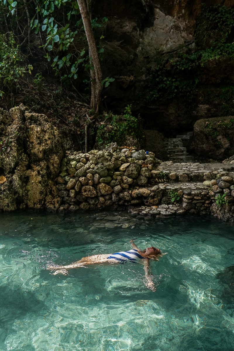 A woman floating in a clear pool of water in a forested area