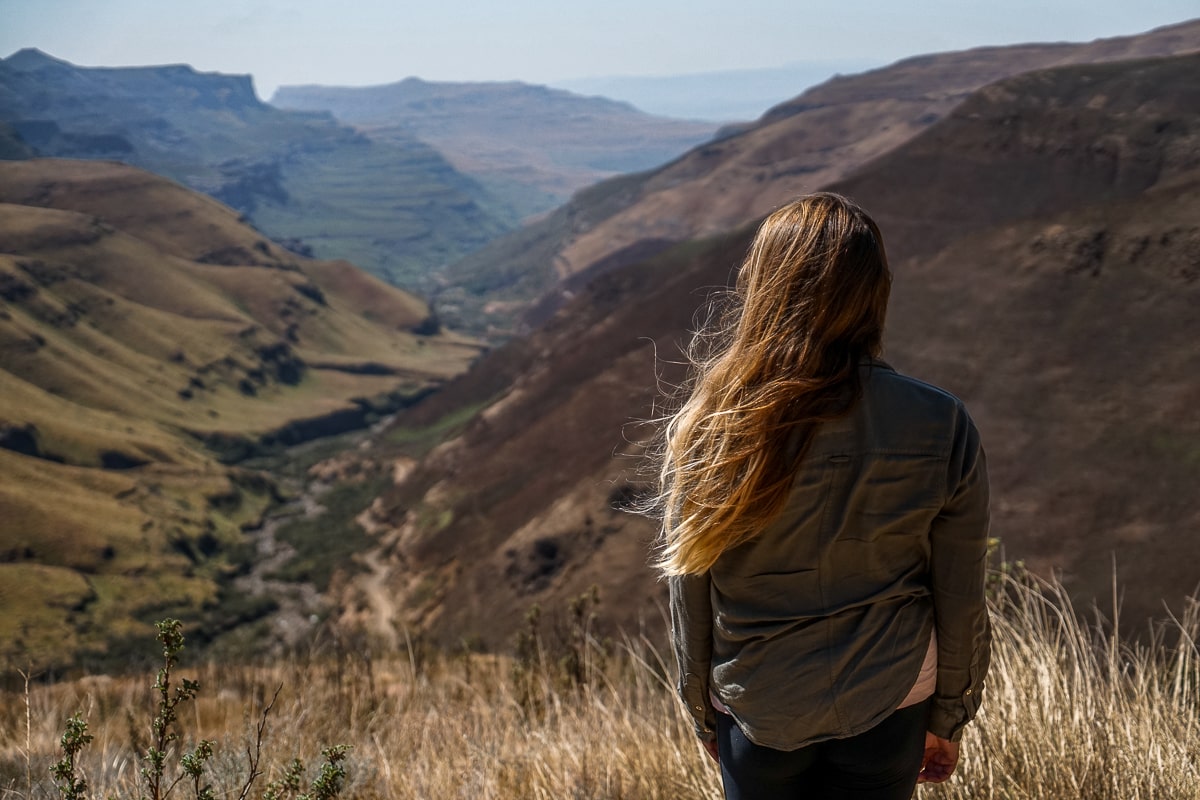 A woman looking down on a valley far below between grassy mountains
