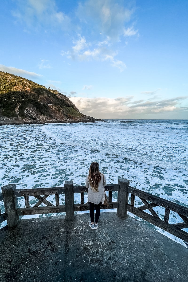 A woman standing on a concrete pier overlooking a foamy sea