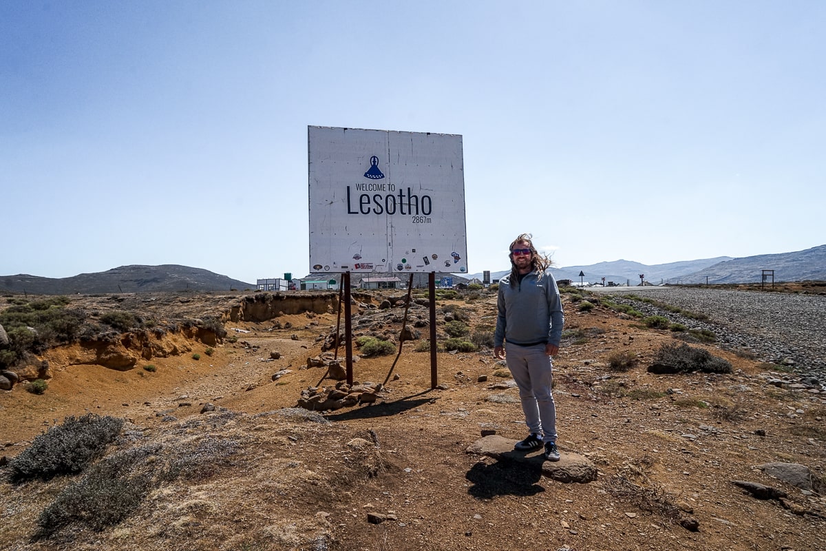 A man standing next to the "Welcome to Lesotho" sign at the top of the Sani Pass