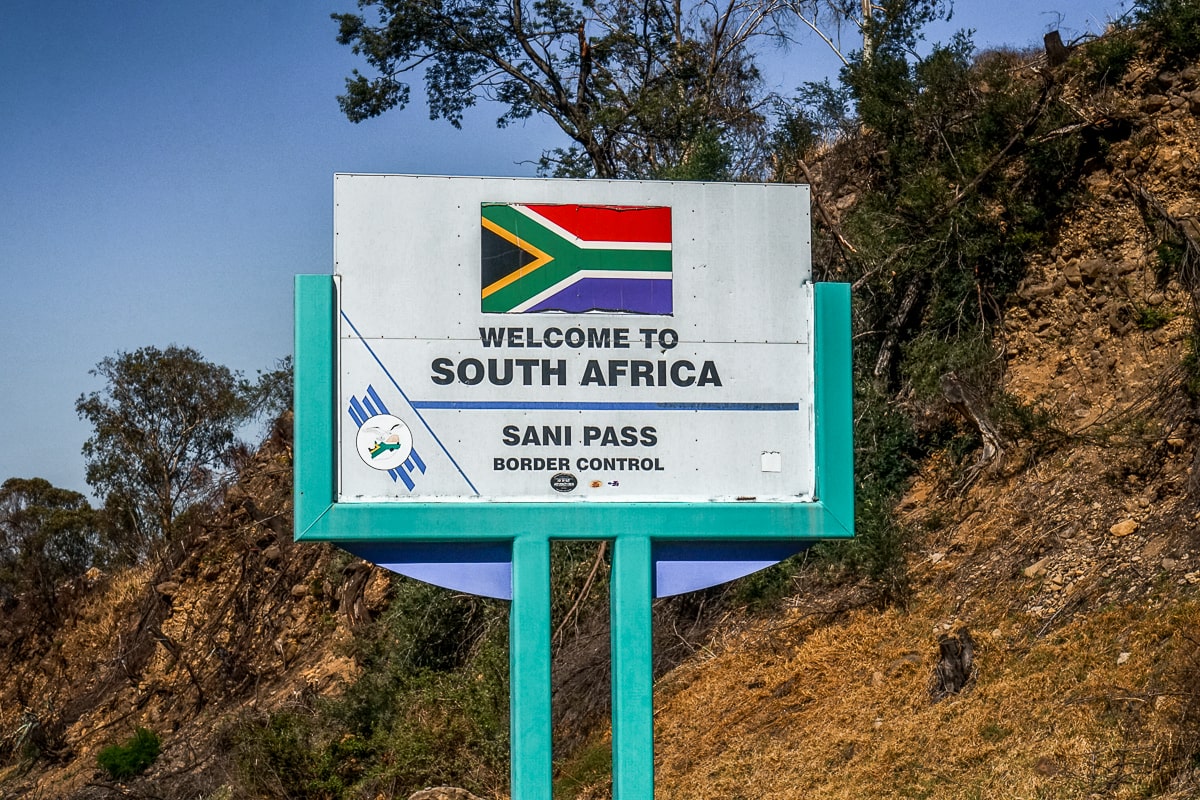 A sign reading "Welcome to South Africa - Sani Pass" featuring the South African flag