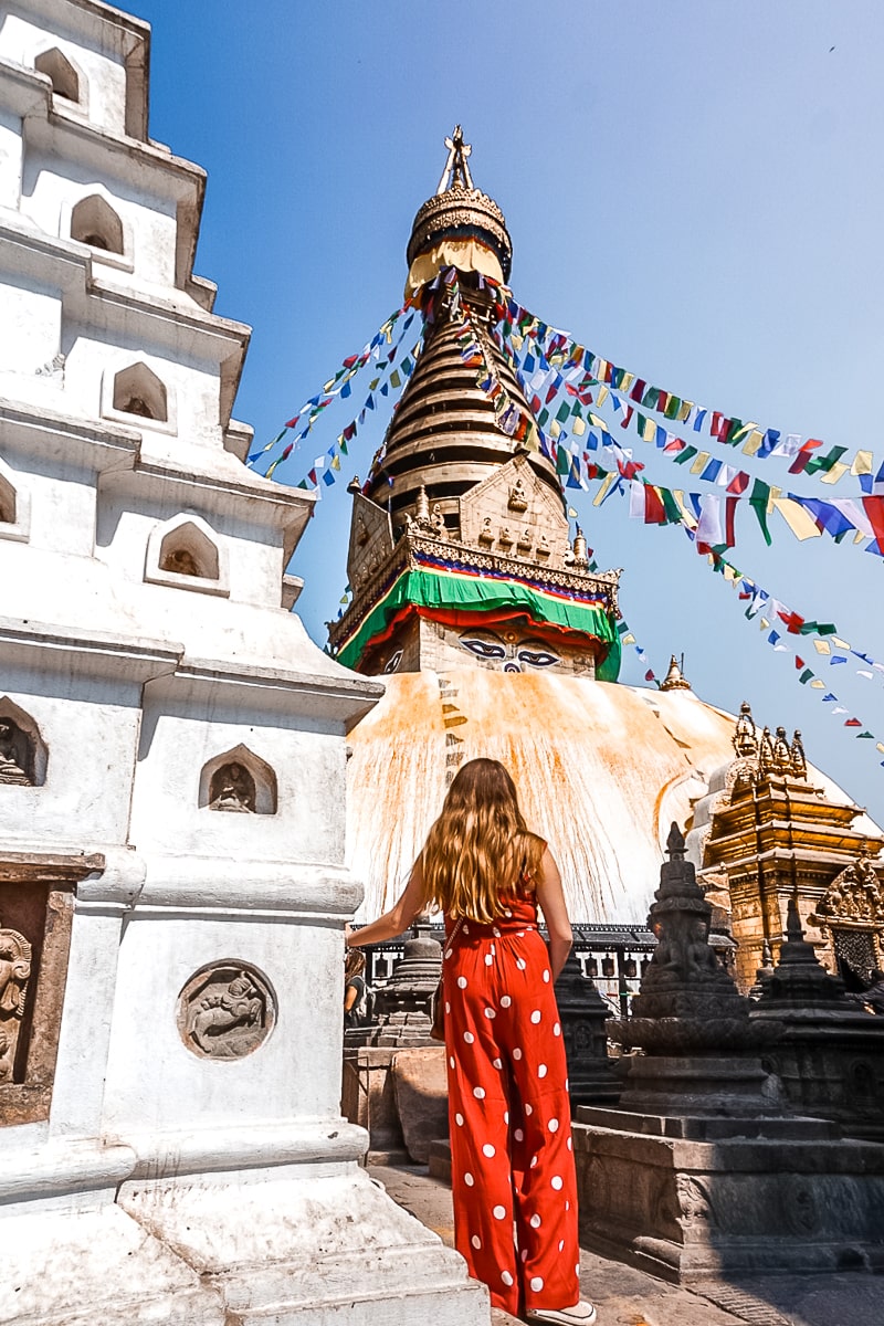 A woman in a red jumpsuit admiring a white and gold buddhist stupa