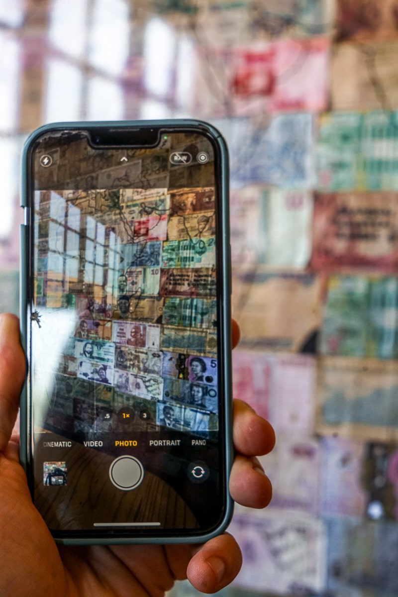 A phone with the camera pointing at a wall of world currencies