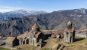 A monastery complex on a grassy hillside with large mountains behind, some dusted with snow
