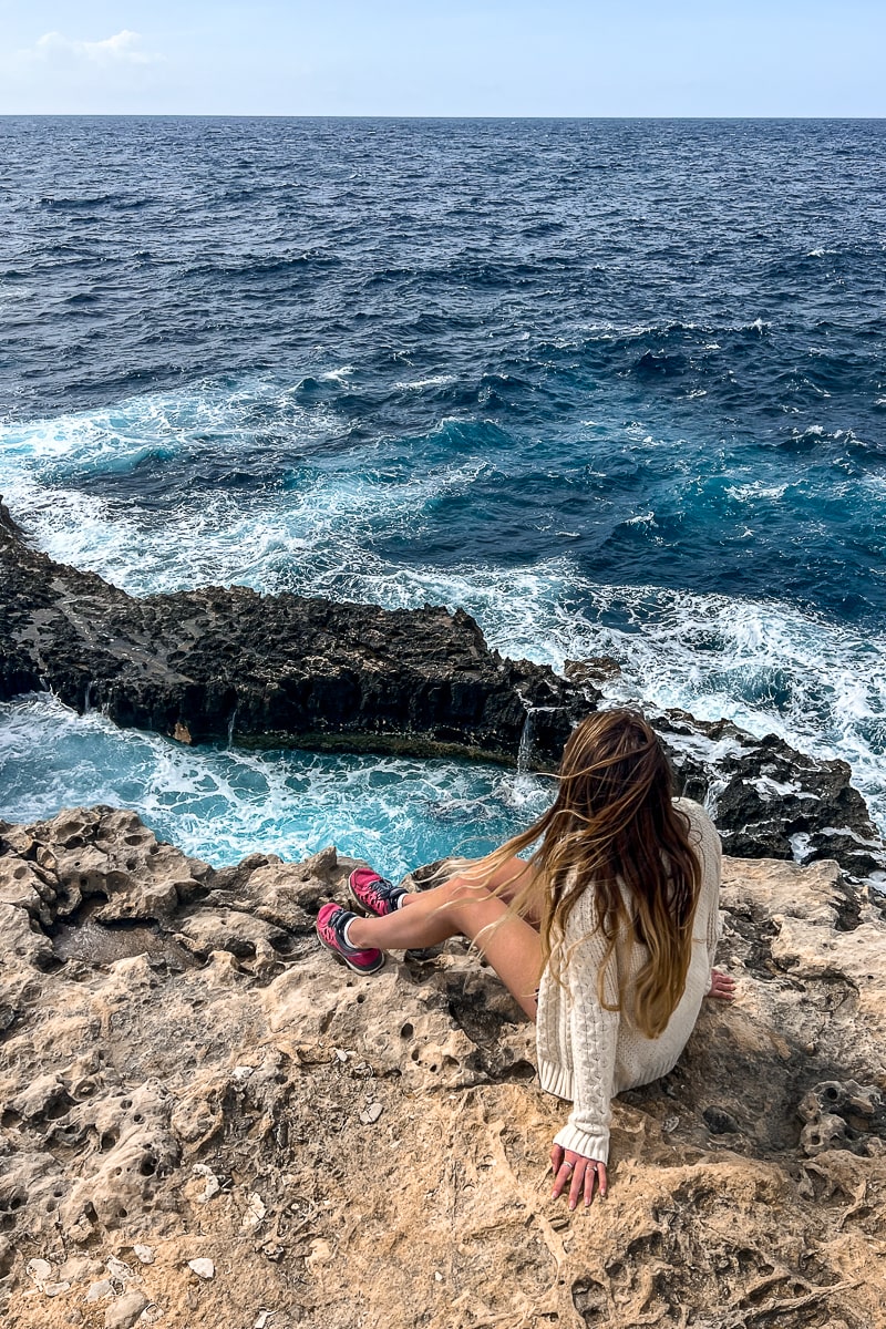 A woman sitting on a rocky cliff with the waves crashing below