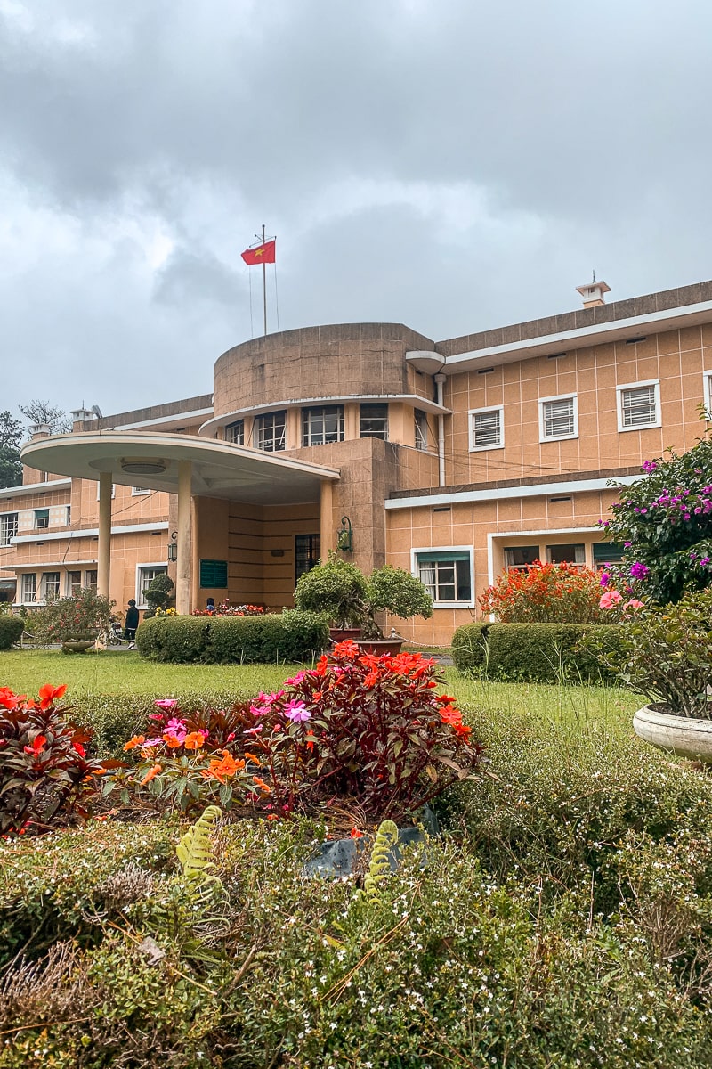 A peach colored summer residence with a vietnam flag flying. A landscaped garden in front