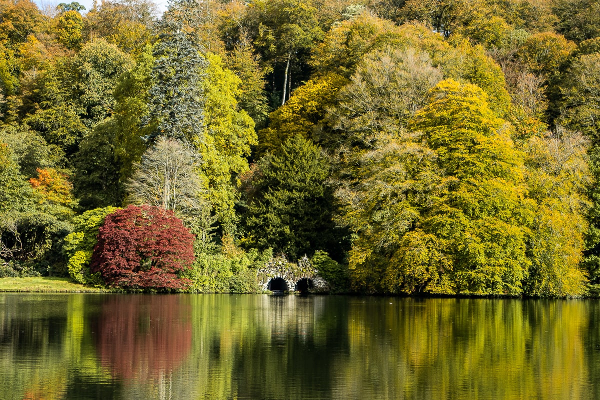 Autumnal coloured trees surrounding a small bridge reflected on a lake