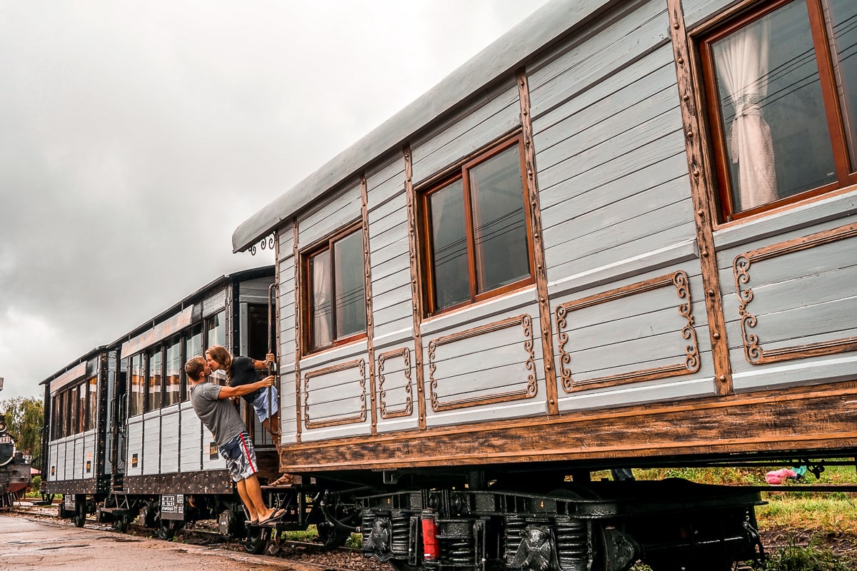 A couple kissing while leaning out of an old train carriage at an outdoor museum