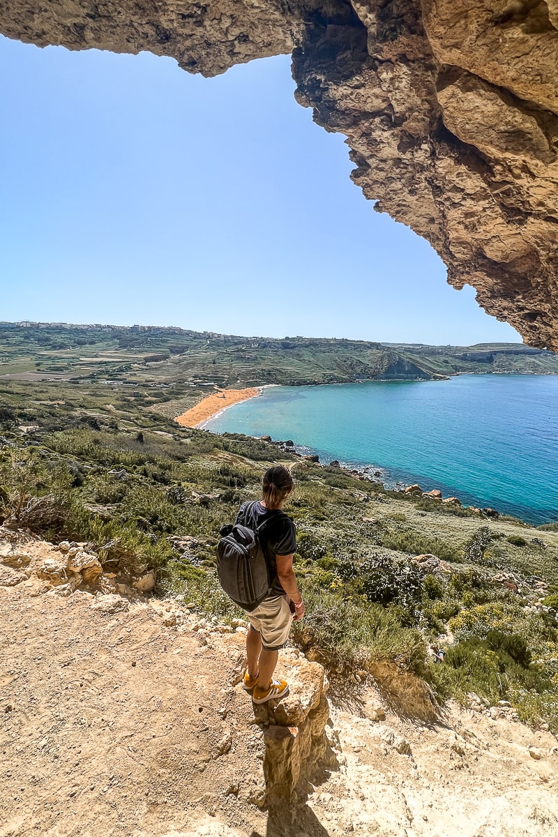 A view looking out from a cave. A man looking out from a cliff to the beach and sea