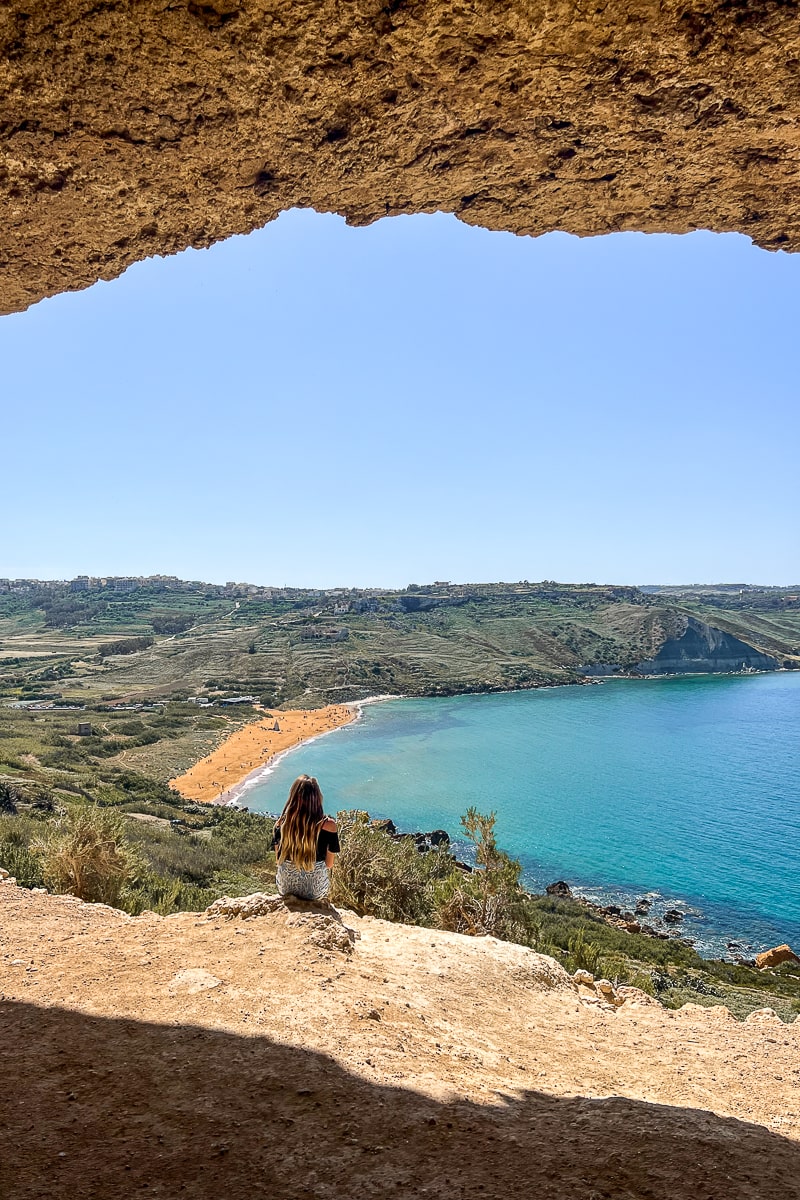 A view looking out from a cave. A woman looking out from a cliff to the beach and sea