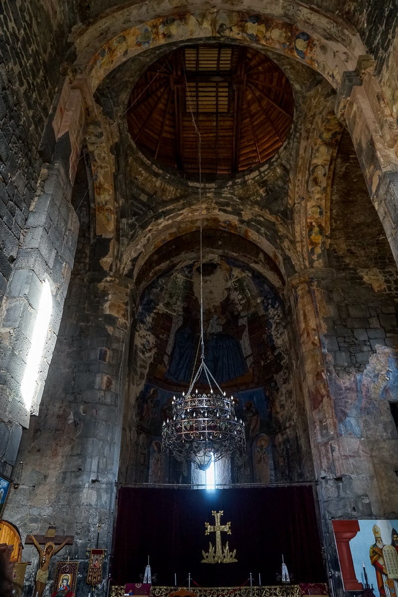 Inside a high vaulted ceiling of a church with a long chandelier dangling above a cross