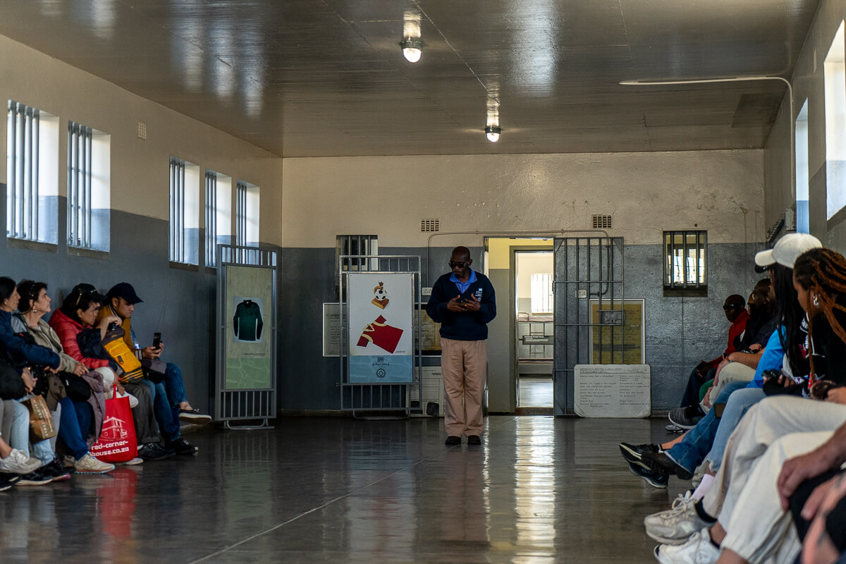 A man giving a talk to a group inside a large communal prison cell