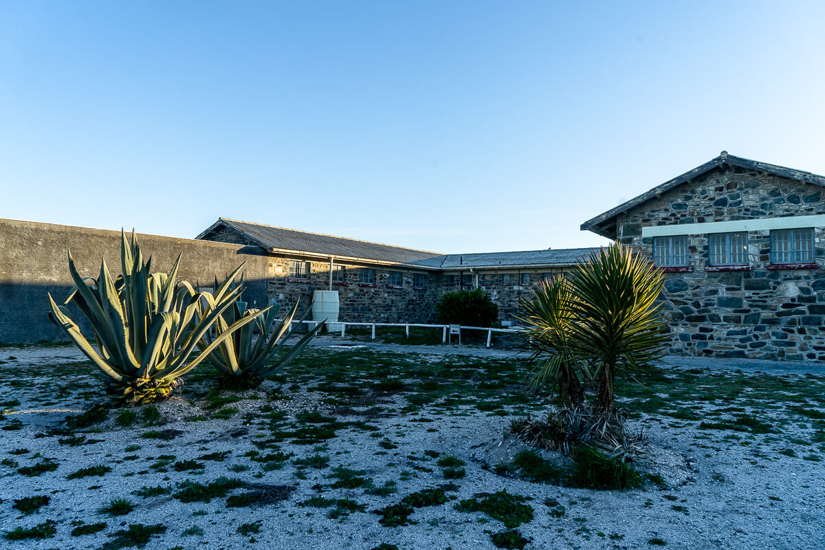 A sandy and grassy yard with a grey stone prison block