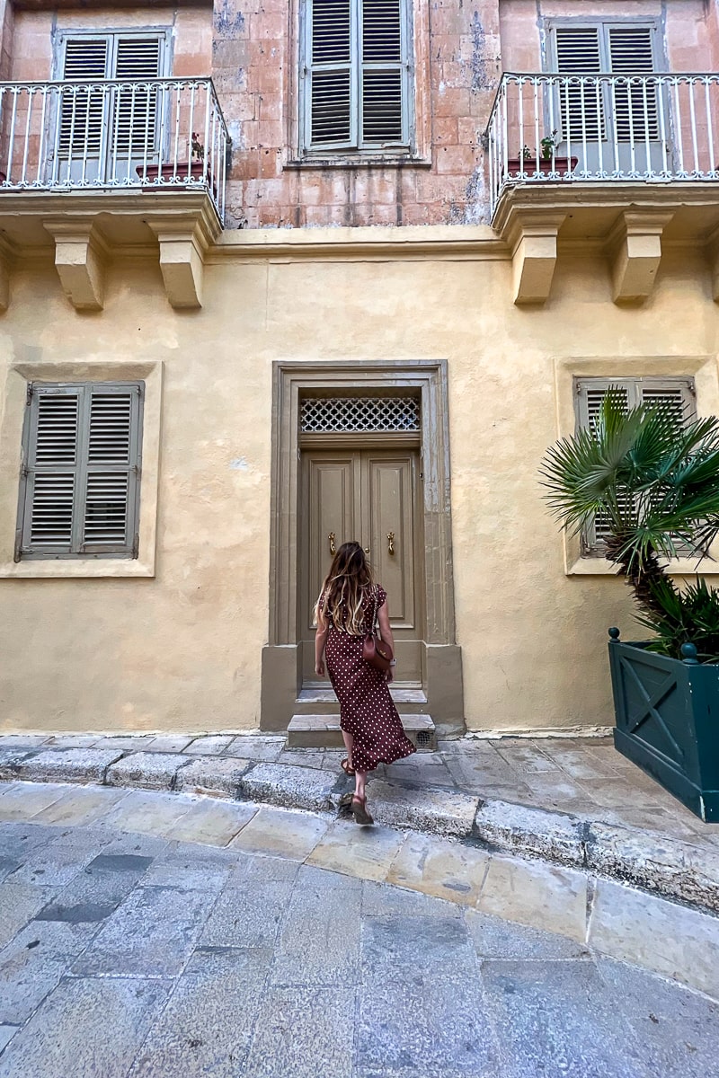 A woman walking towards a khaki colored door in a pretty street