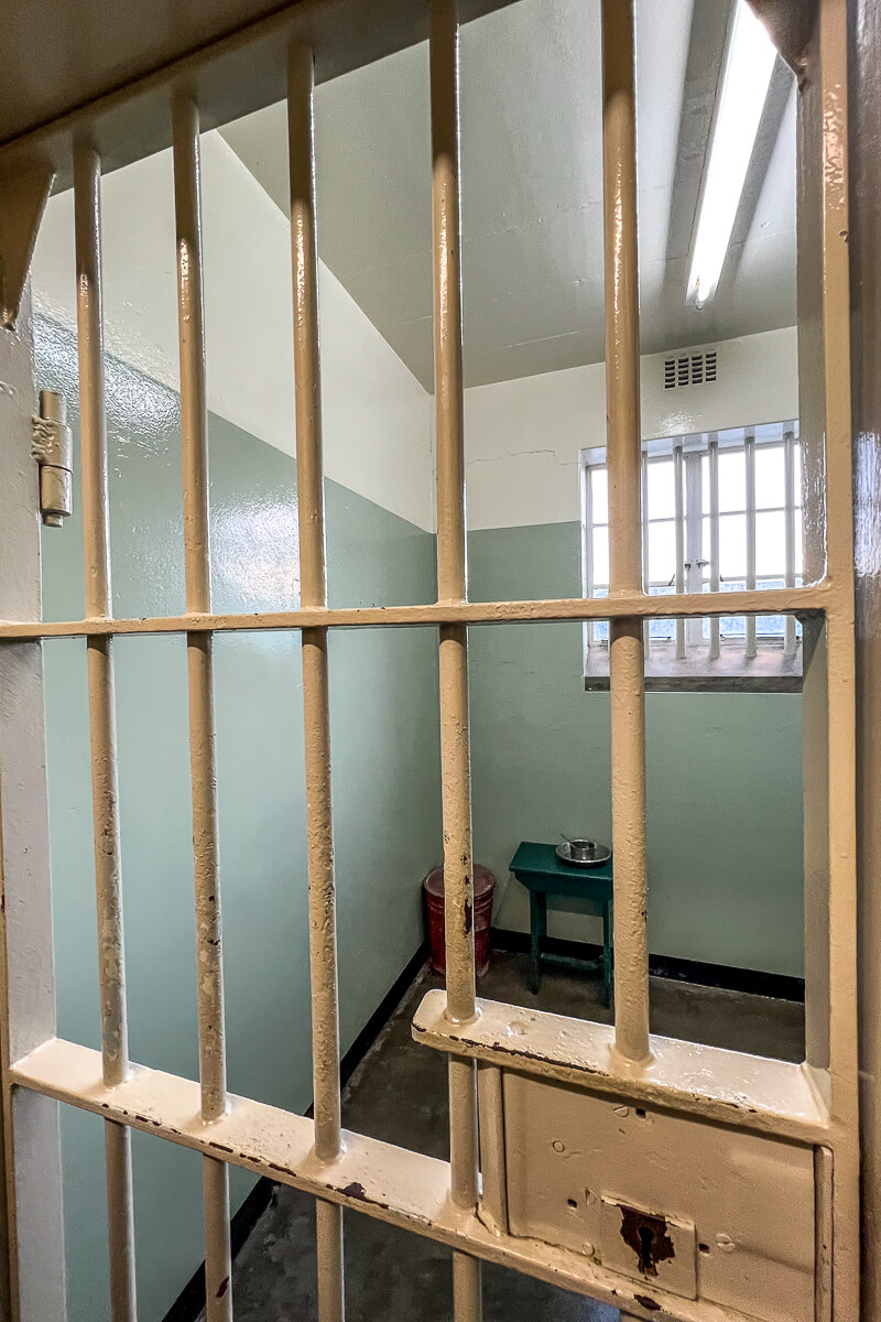 A small prison cell behind a locked door with stool in the corner