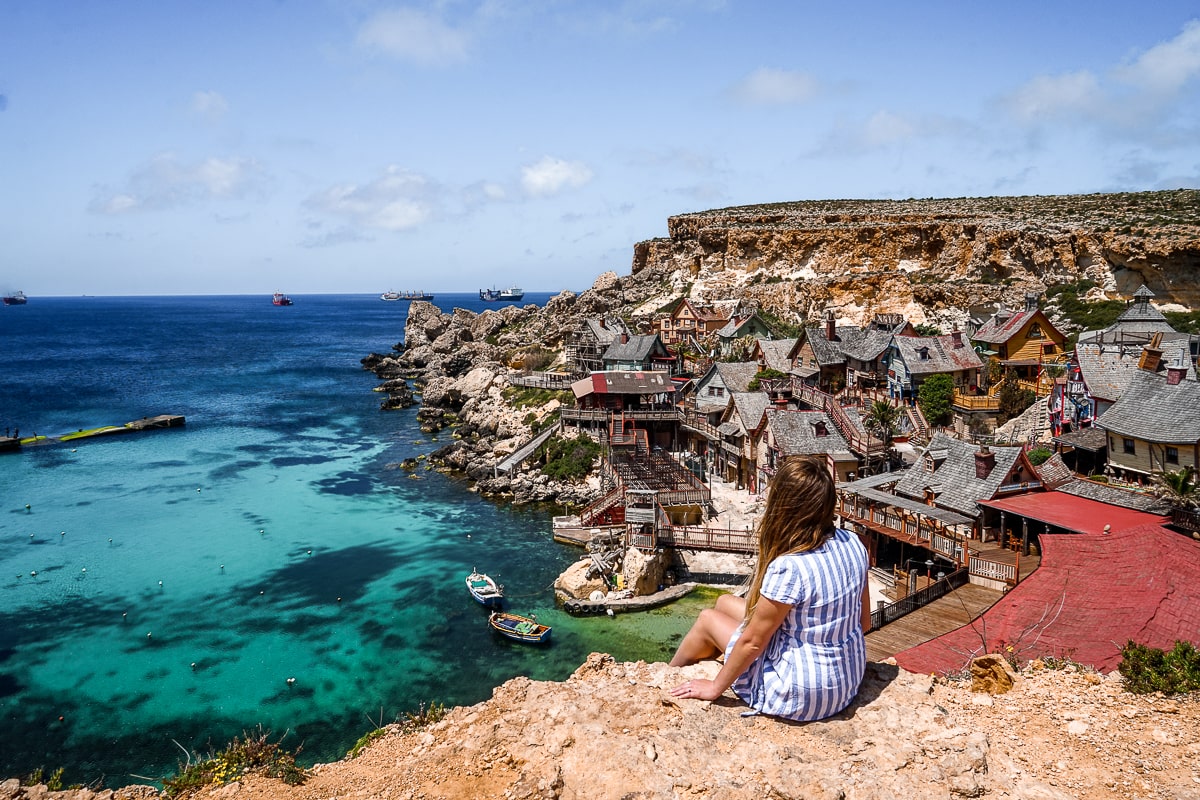 A woman sitting on a cliff overlooking a movie set of a Popeye village