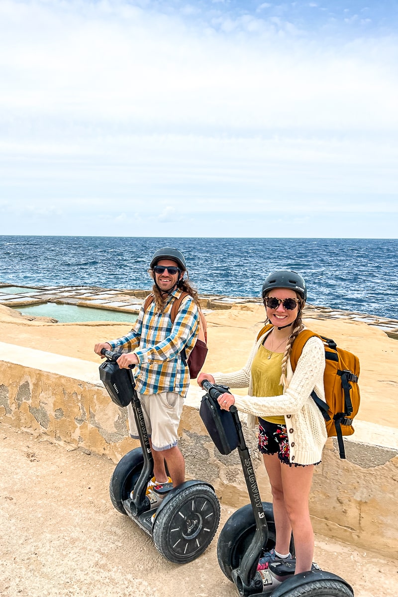 A couple stood on Segways with man-made salt pans and the sea behind