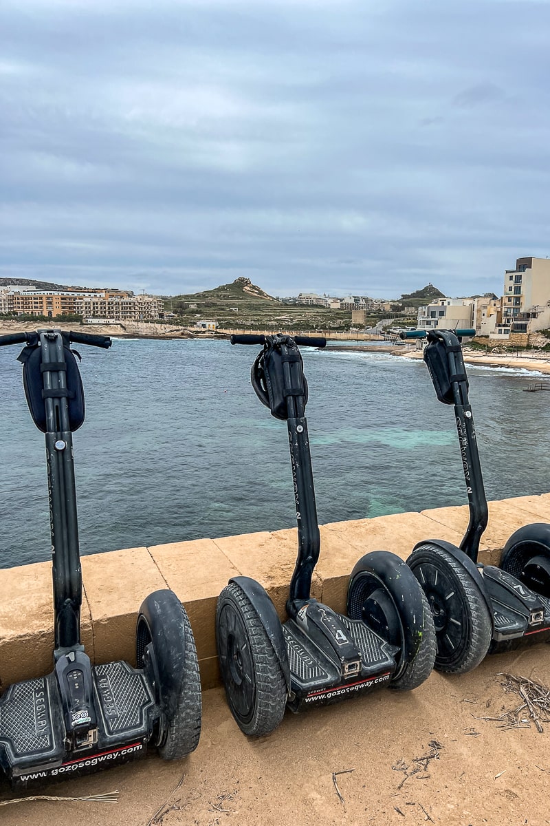 A row of Segways leaning against a low wall next to the sea