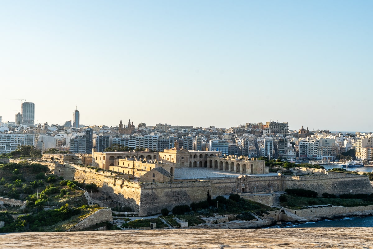 A sand colored stone fort with a modern city behind