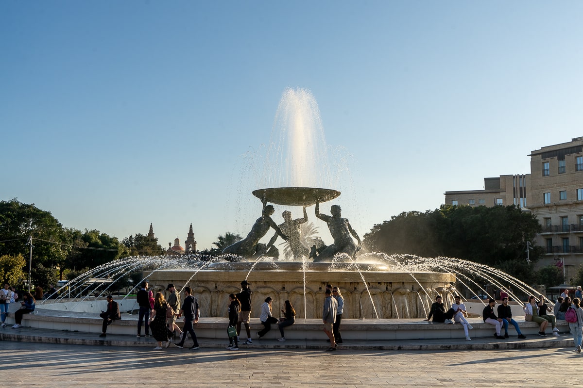 A large fountain with statues of three people holding a large plate up