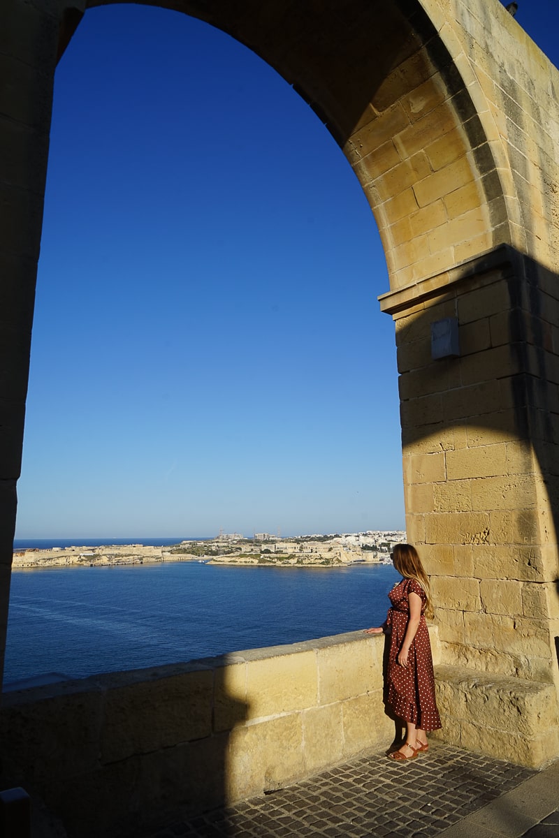 A woman looking out from a stone archway over the sea in Valletta
