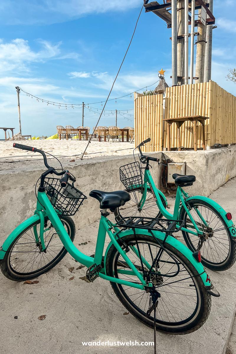 Two mint green bikes with baskets parked next to the beach