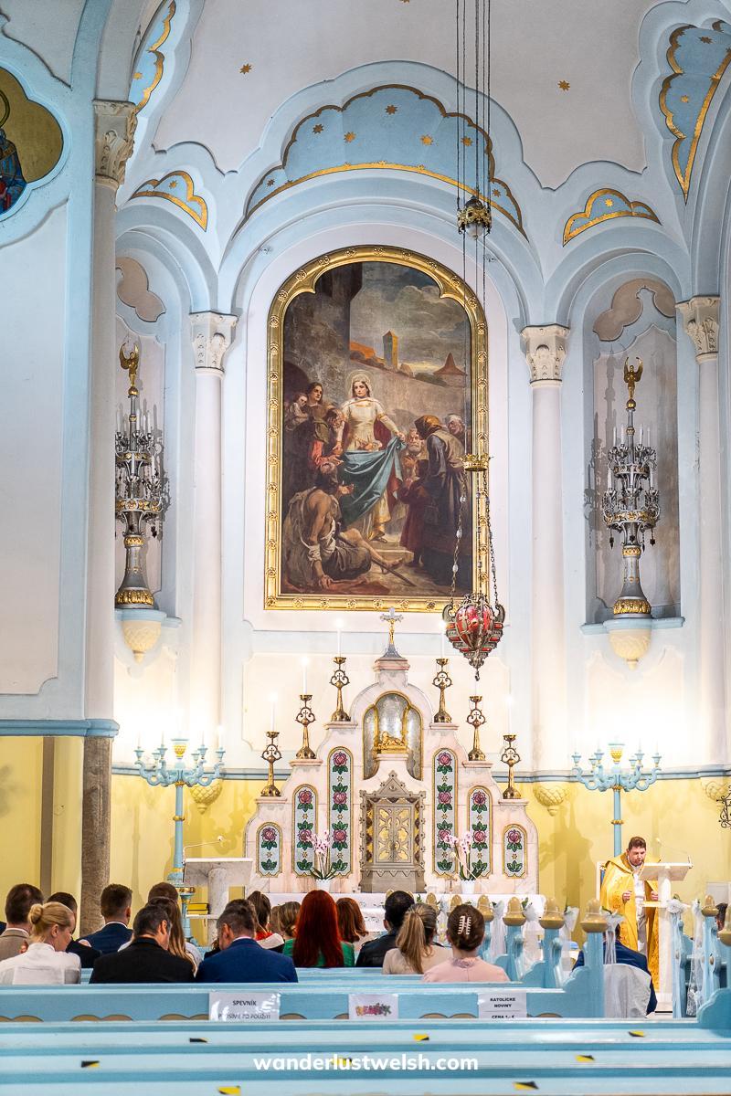 Inside a sky blue and baby yellow art nouveau church with large oil painting