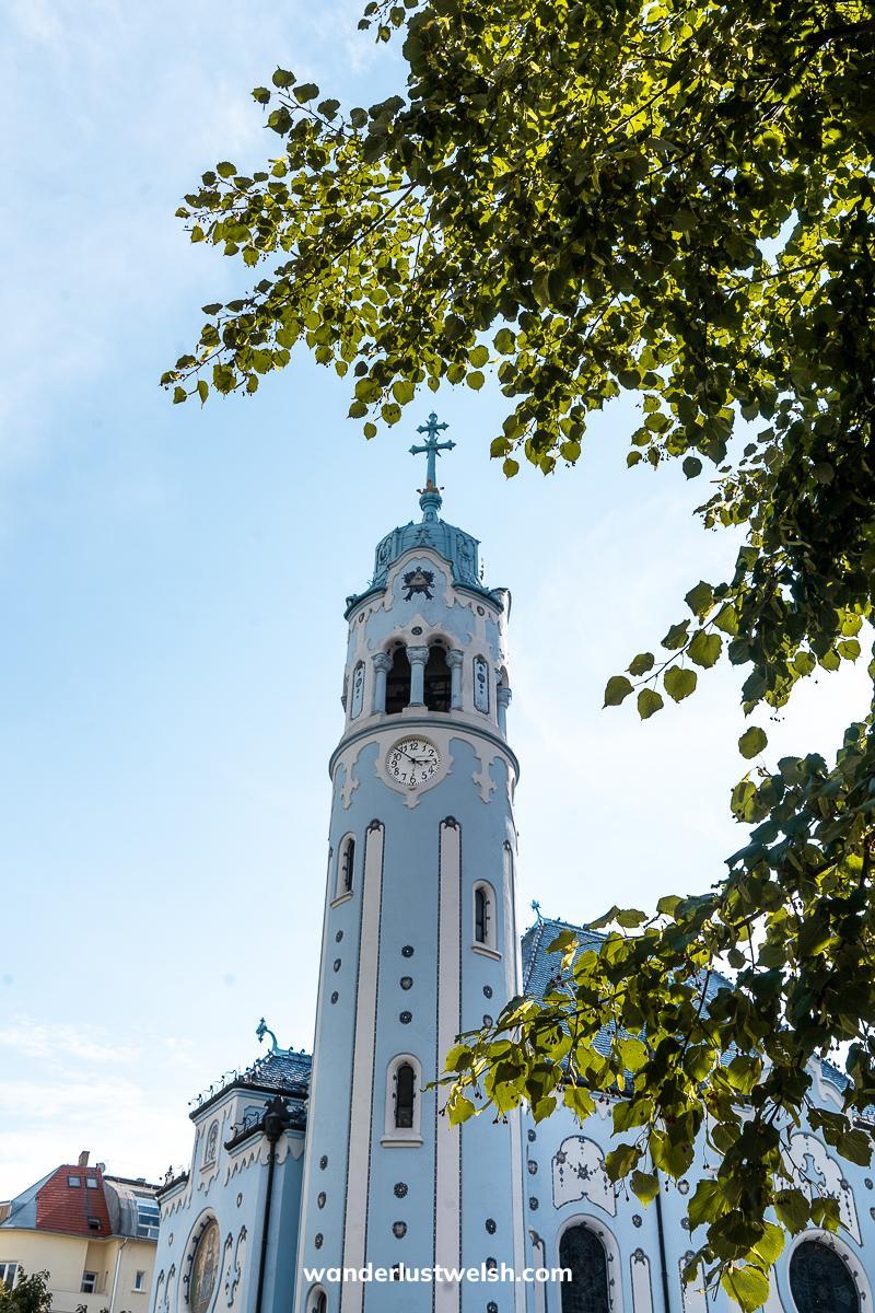 A sky blue art nouveau church framed by trees