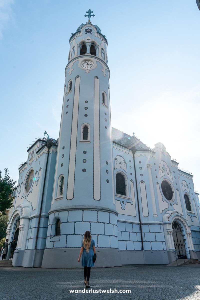 A woman looking up at a blue art nouveau church