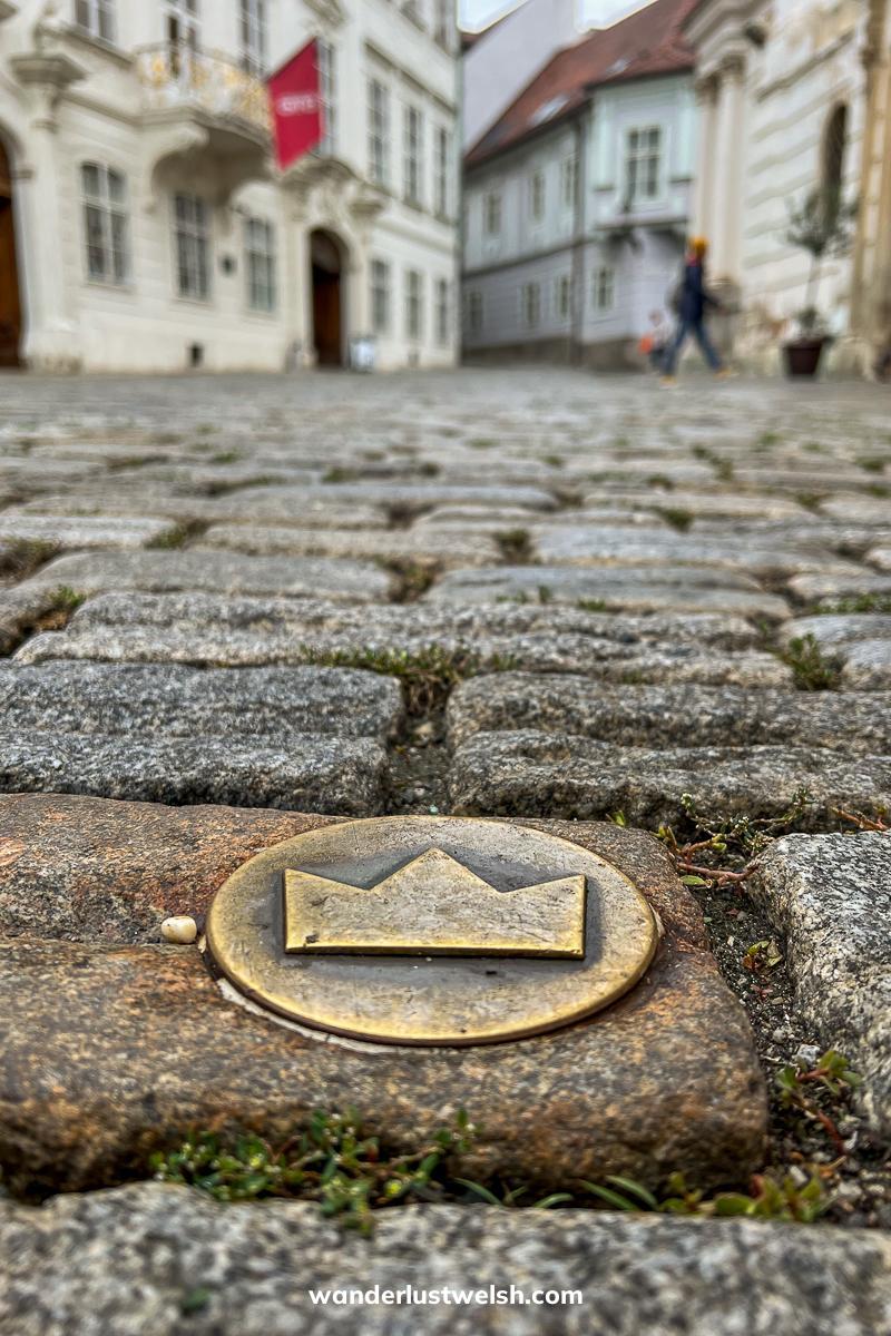 A bronze emblem of a crown in a circle on a cobbled street