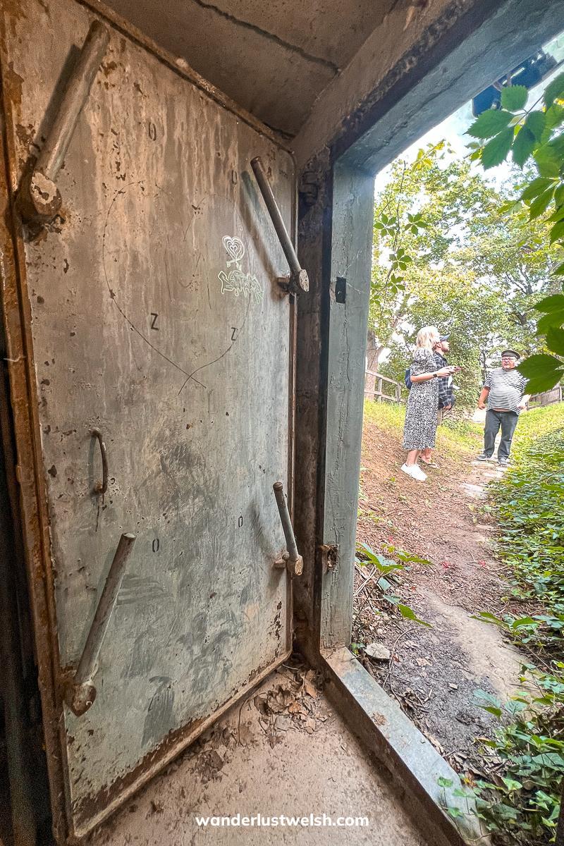 An open doorway leading out of a secret bunker, two people standing in the grass outside
