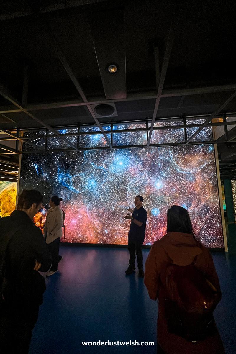A man giving a talk in front of a colorful photo of gas clouds and star formations
