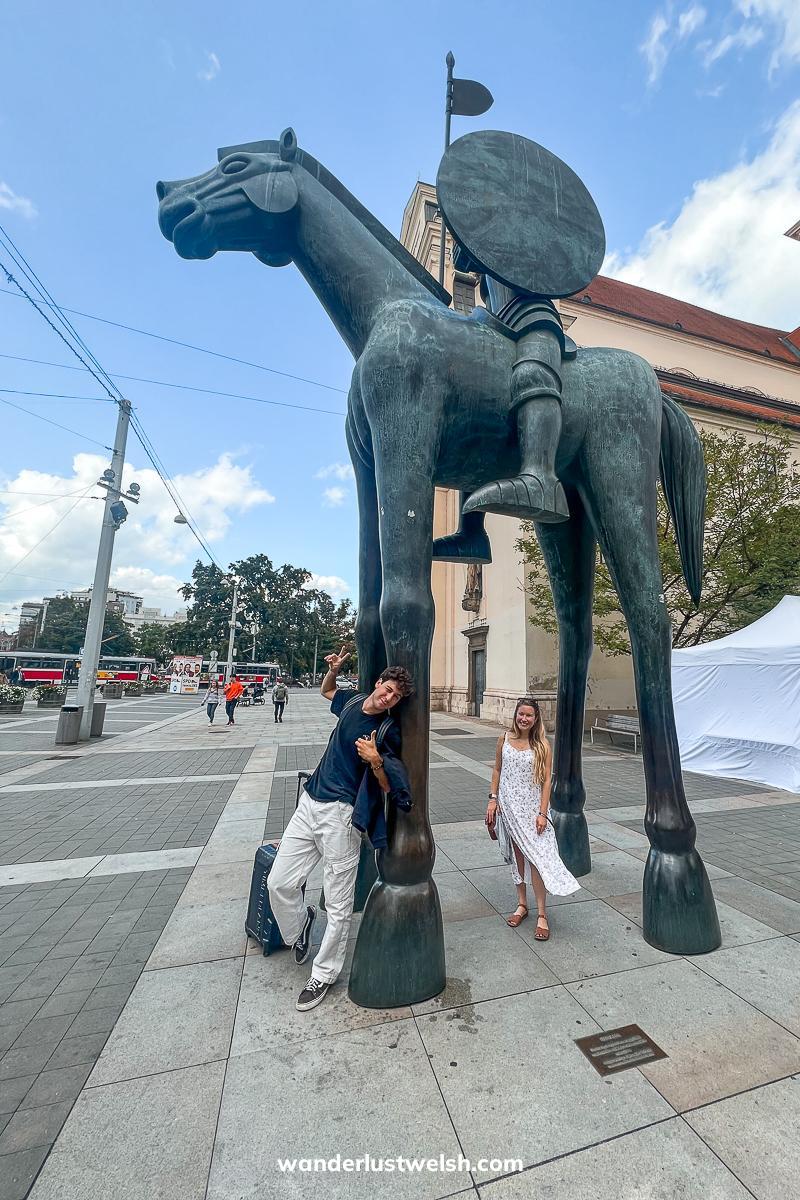 Two friends standing under a large statue of a horse and rider