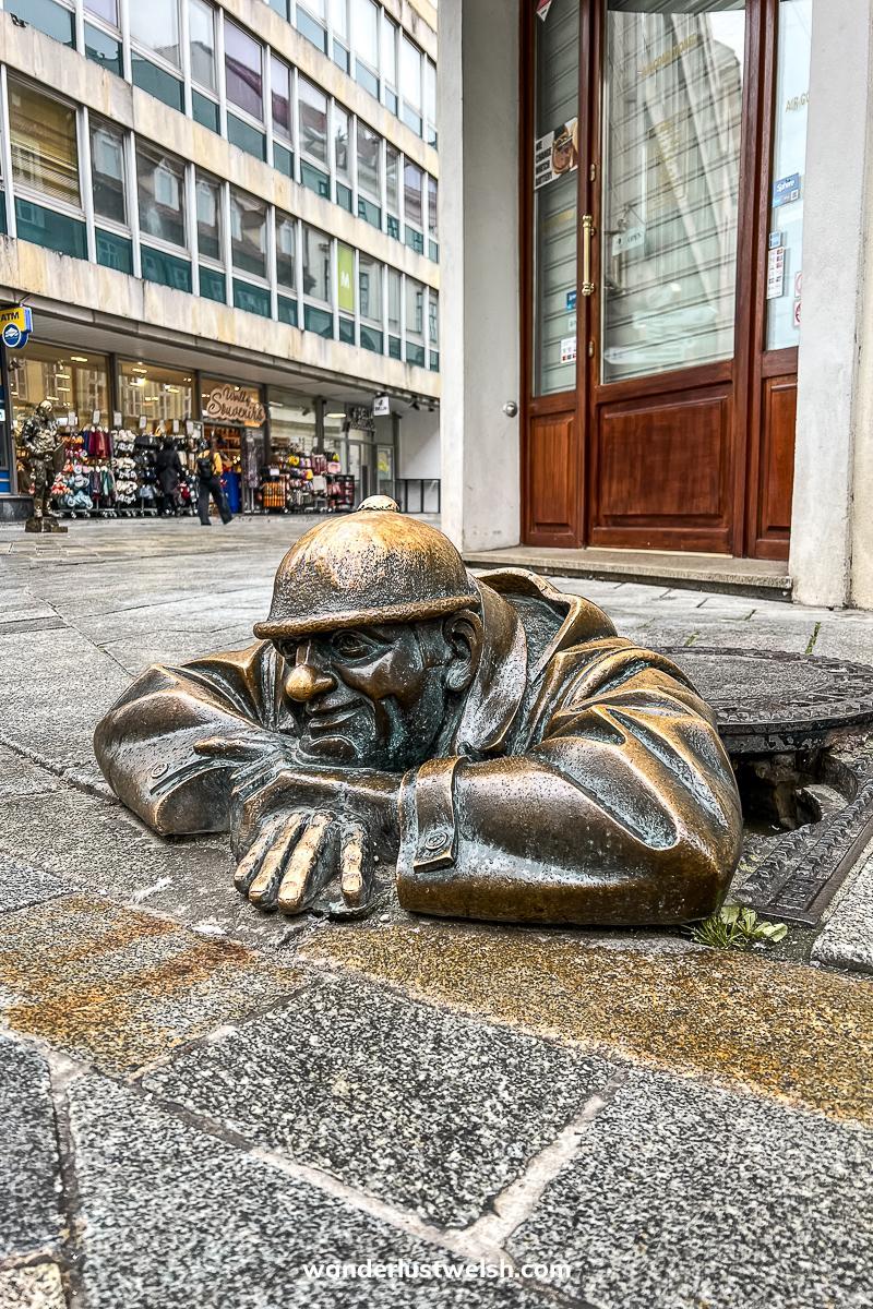 A bronze sculpture of a man climbing out of a manhole cover