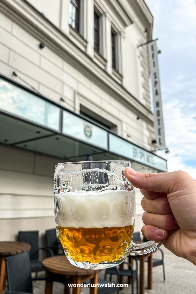 Someone holding a Czech beer in a tankard style pint glass in front of a bar