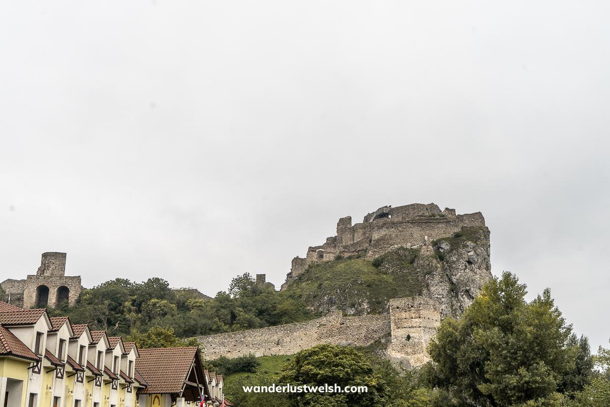 A ruined castle on a hillside with modern rooftops in the foreground