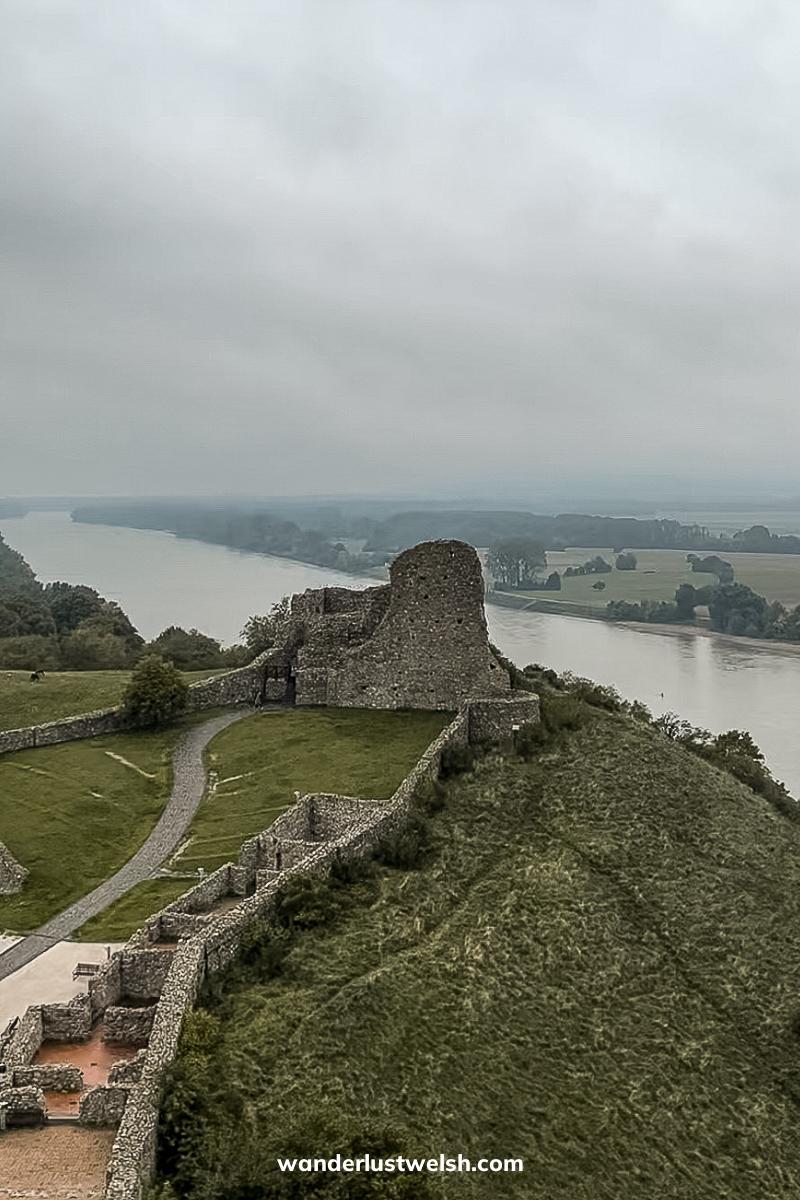 A partially ruined castle tower with walls on a rounded hill overlooking the Danube river