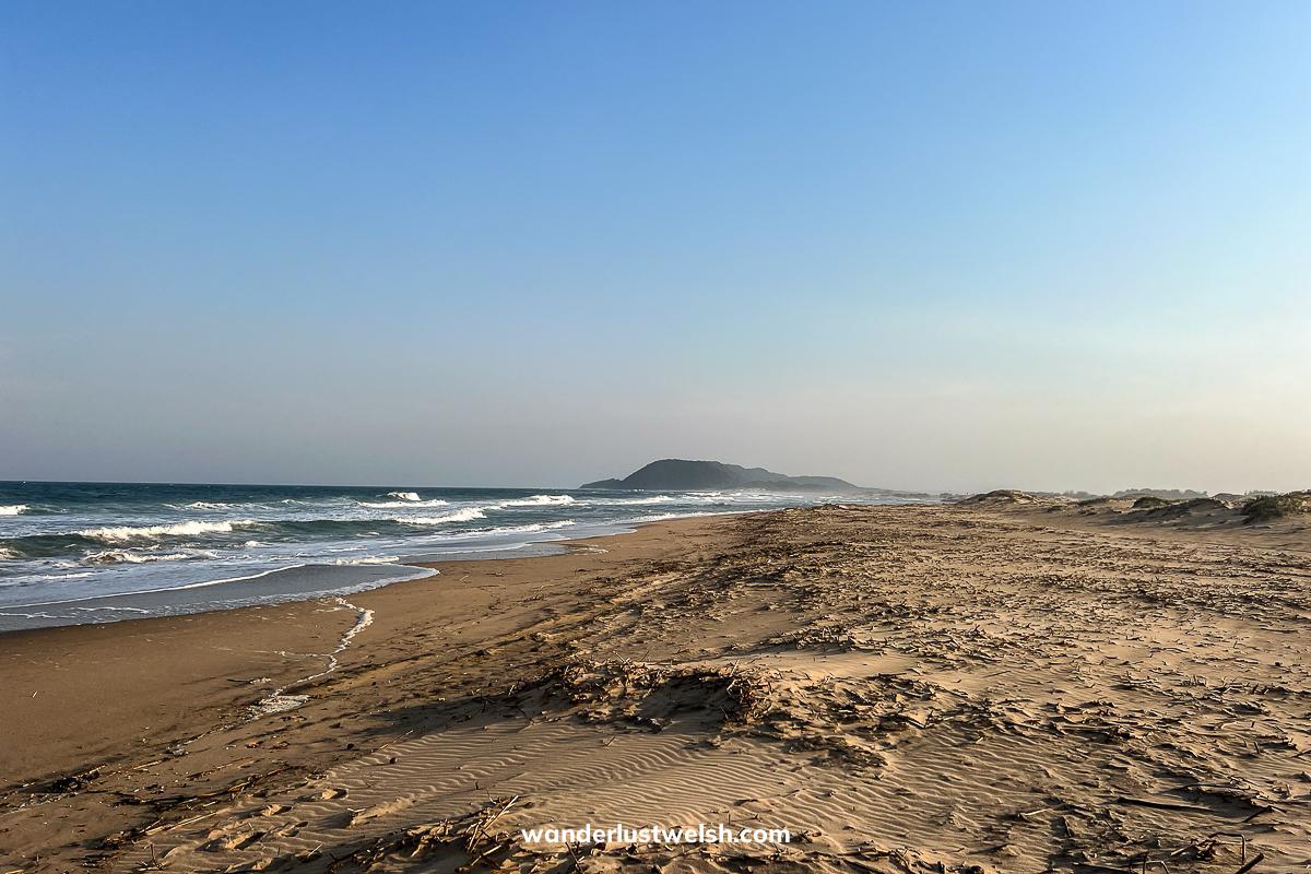 A long sandy beach with nothing around, frothy waves braking on the shore